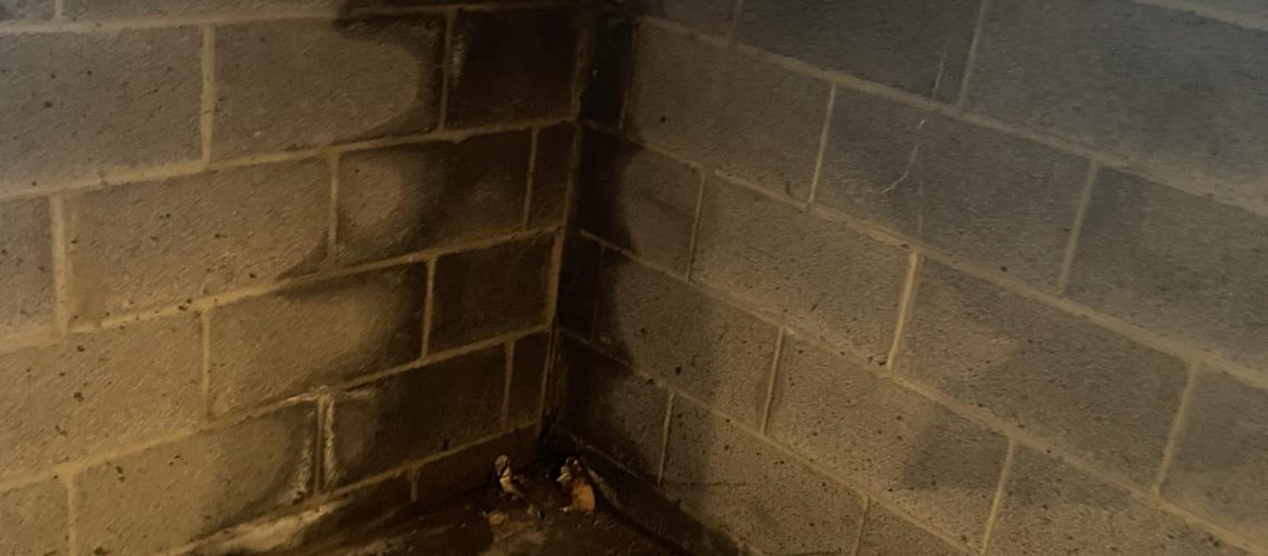 Basement corner showing water stains on cinder block walls, highlighting the need for professional waterproofing services to prevent water damage.